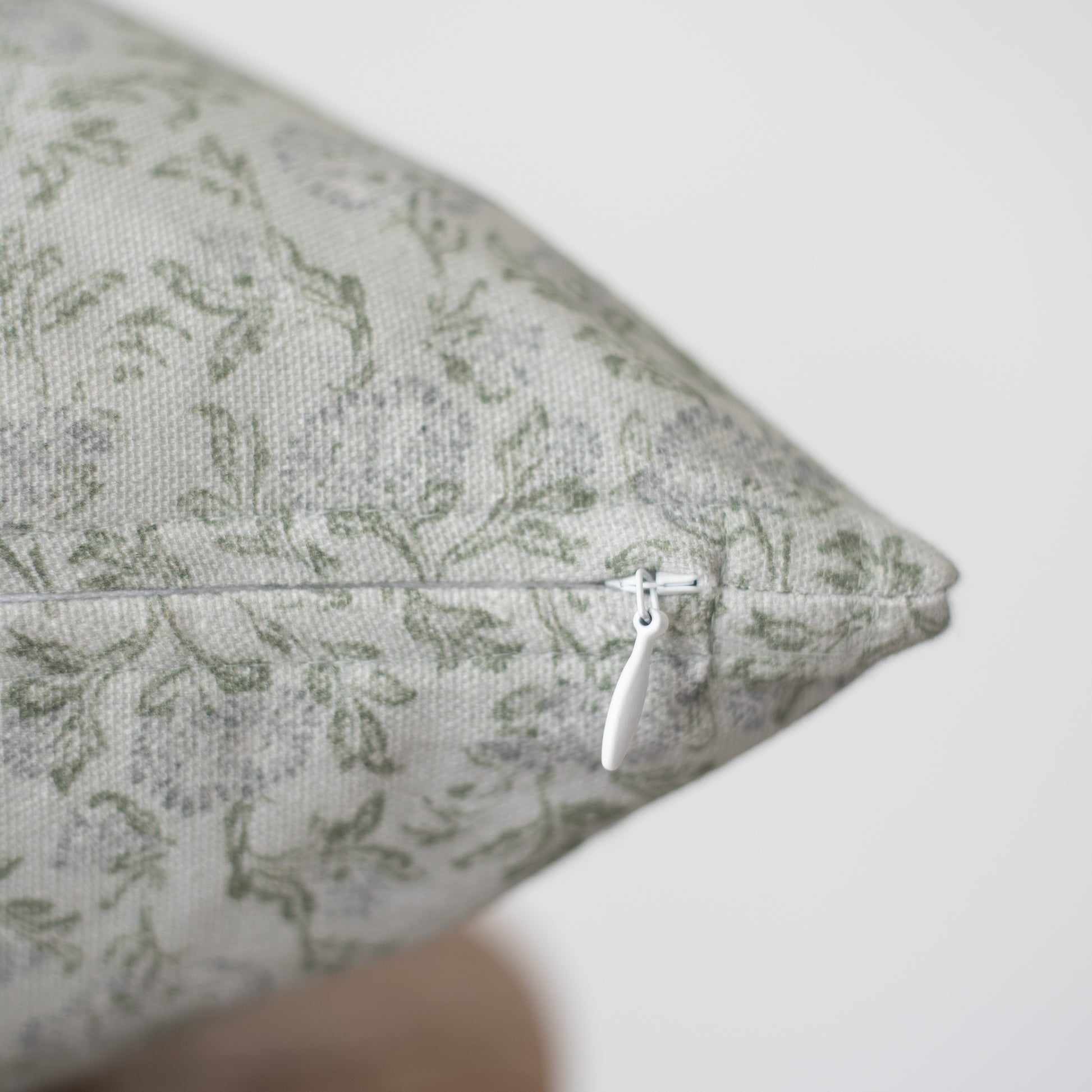 Beige linen pillow with sage green damask pattern and white zipper closure.