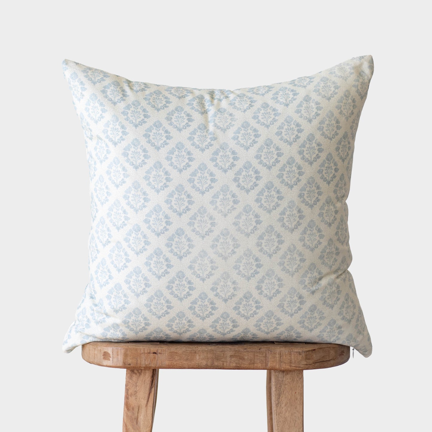 Light blue damask patterned pillow cover displayed on a wooden stool.
