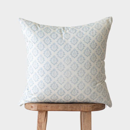 Light blue damask patterned pillow cover displayed on a wooden stool.