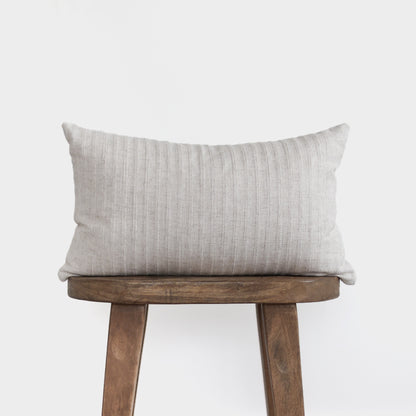 Light gray striped lumbar pillow displayed on wooden stool against white background.