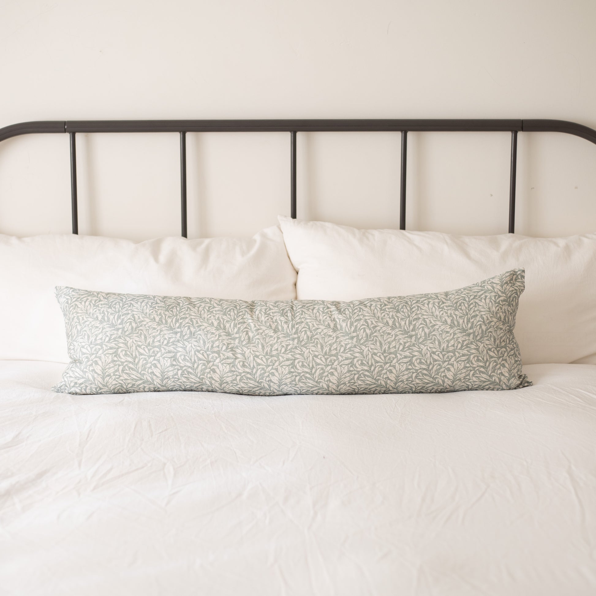 Rectangular lumbar pillow with sage green leaf print on white bedding against metal headboard.