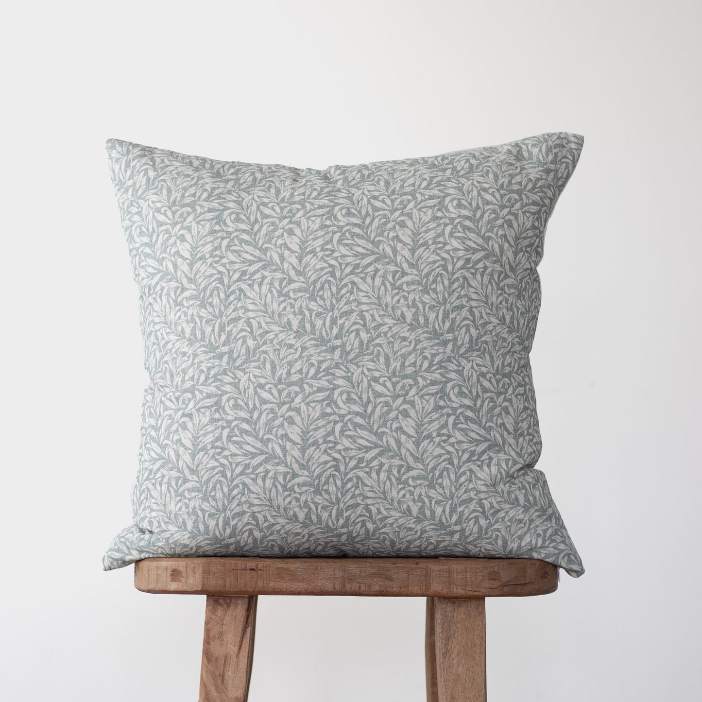 Gray and white leaf-patterned throw pillow displayed on a wooden stool.