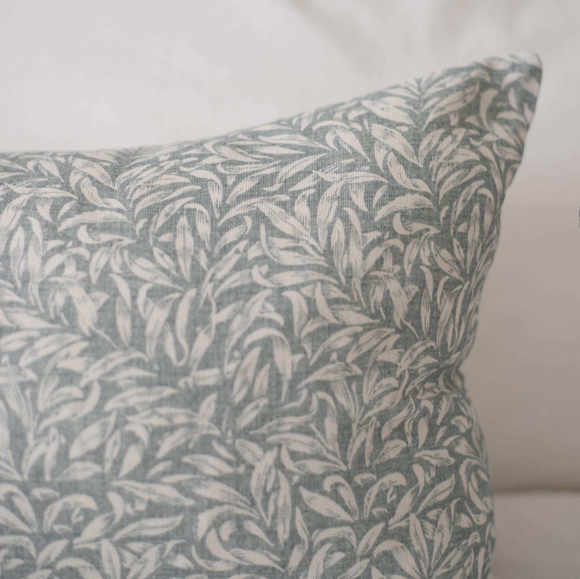 Gray and cream leaf pattern pillow with woven texture visible on corner against neutral background.