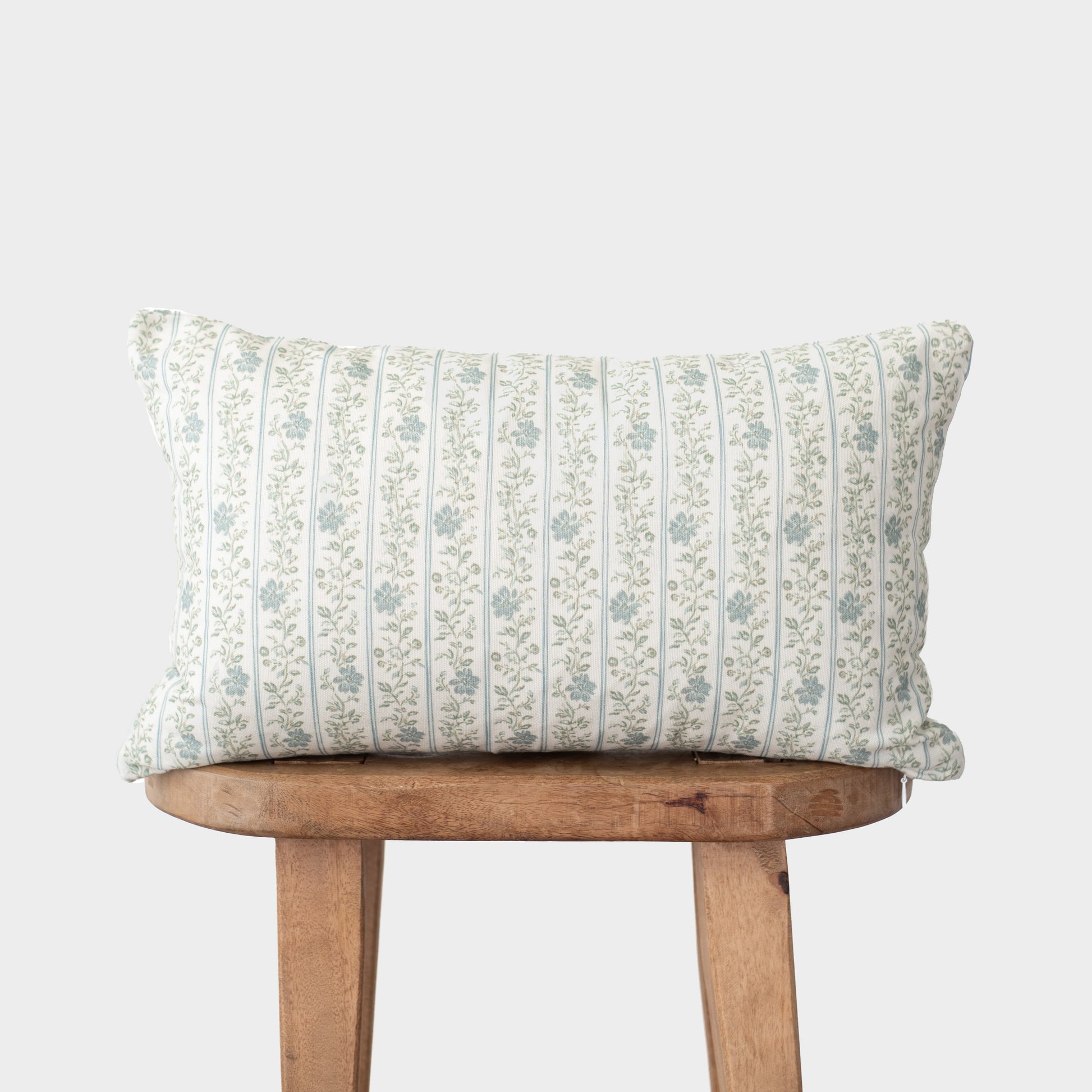 Cream-colored pillow with blue vertical striped floral pattern on wooden stool.