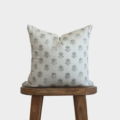 Cream pillow cover with gray floral pattern displayed on wooden stool.