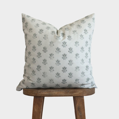 Cream linen pillow with small blue floral pattern, displayed on wooden stool.