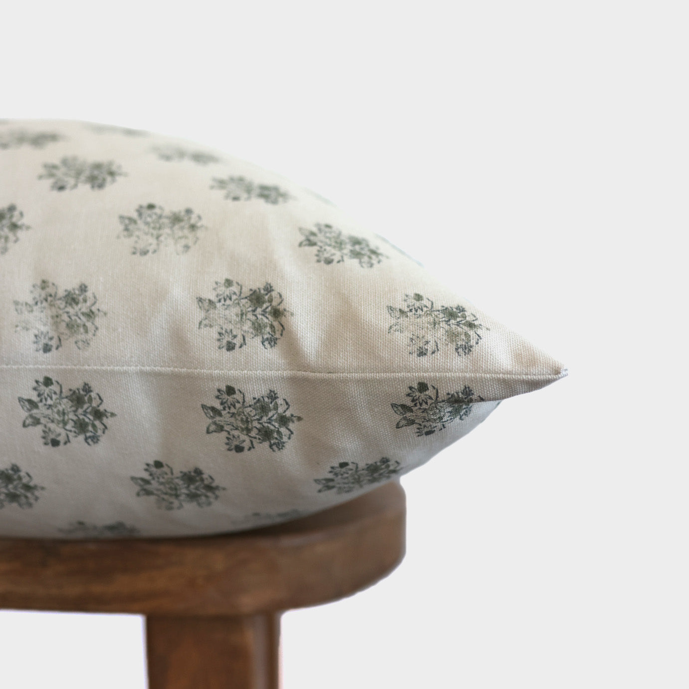 Cream pillow with gray floral pattern resting on wooden stool.