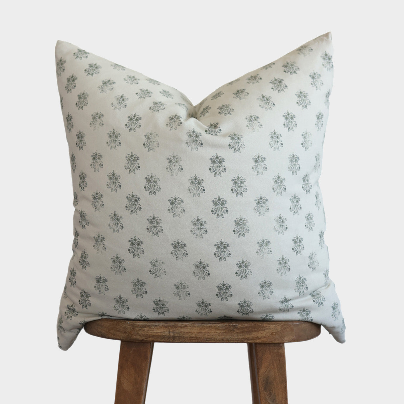Cream-colored pillow with small gray floral pattern displayed on wooden stool.