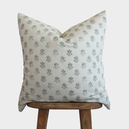 Cream-colored pillow with small gray floral pattern displayed on wooden stool.