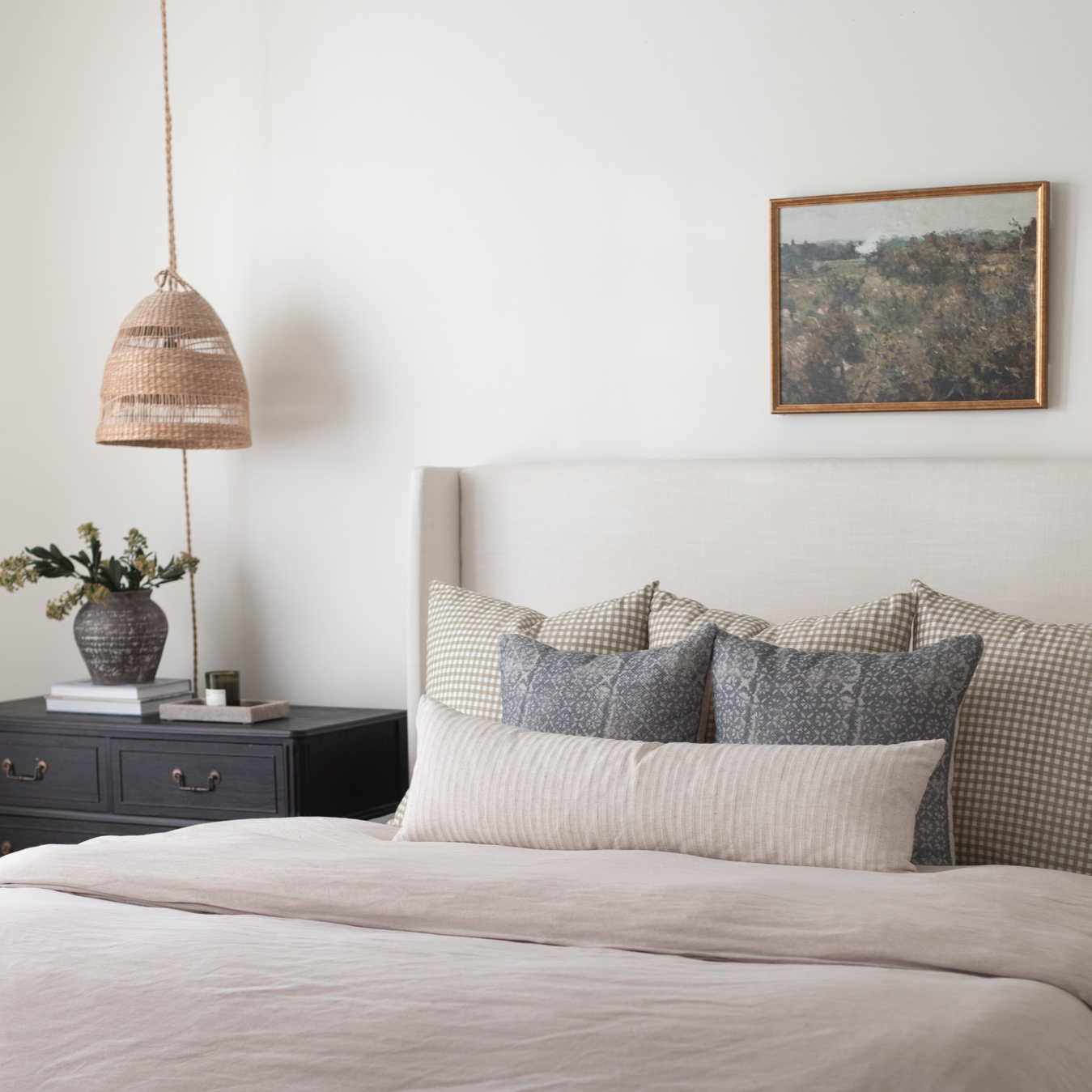 Framed landscape photograph with wooden border hung on white bedroom wall above bed with checkered pillows.