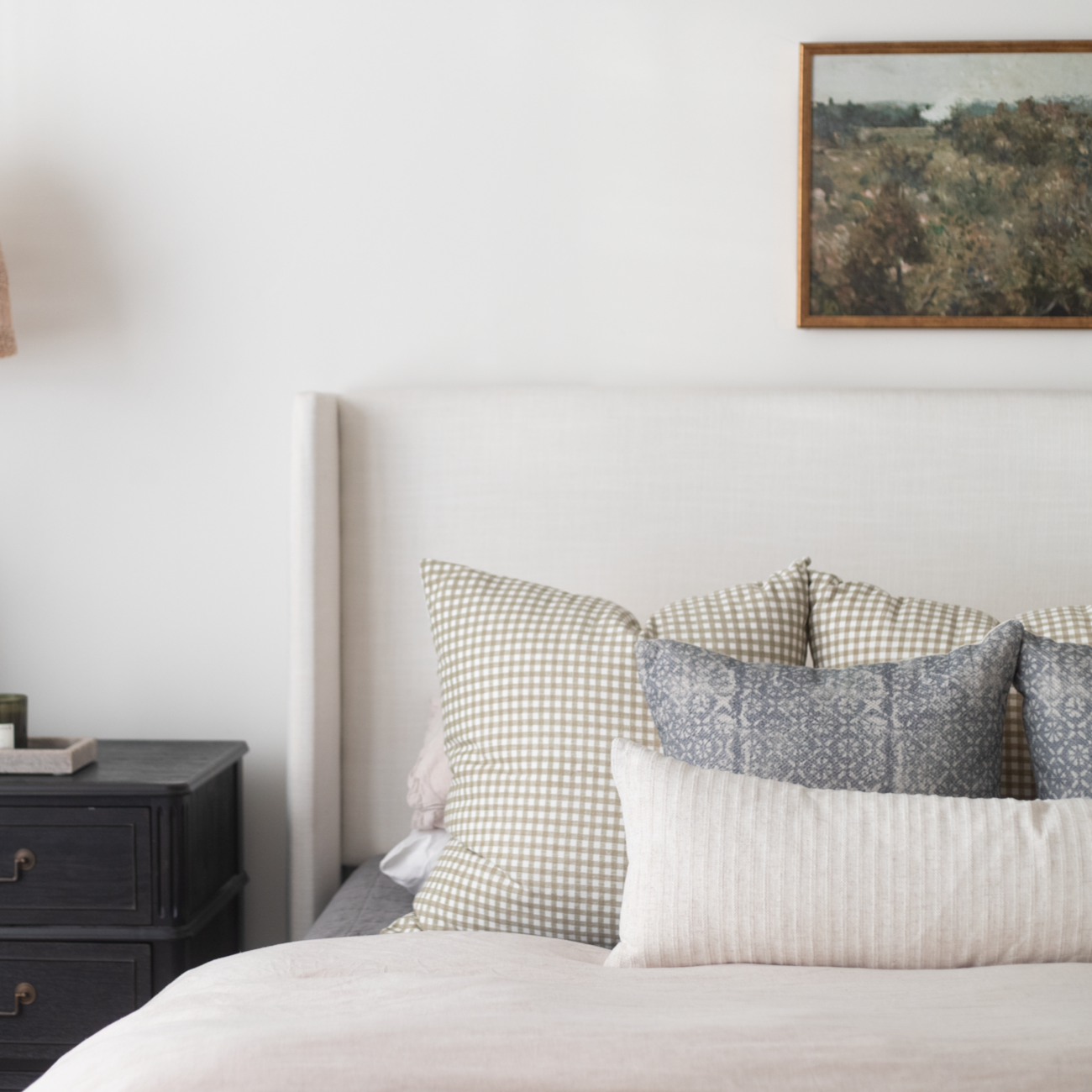 Framed landscape artwork with brown wood frame hanging above a bed with patterned pillows.