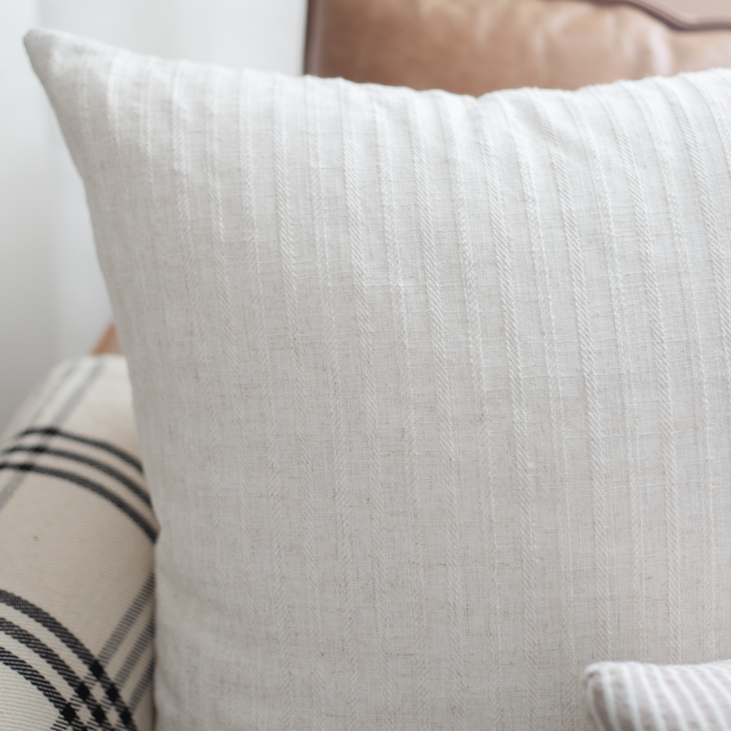 White textured throw pillow with vertical ribbed pattern, displayed on bed with striped pillows.