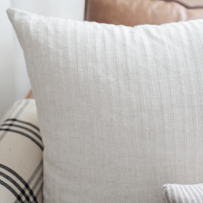 White textured throw pillow with vertical ribbed pattern, displayed on bed with striped pillows.