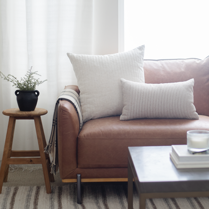 Rectangular cream and striped lumbar pillows arranged on a cognac leather sofa in a styled living room setting.