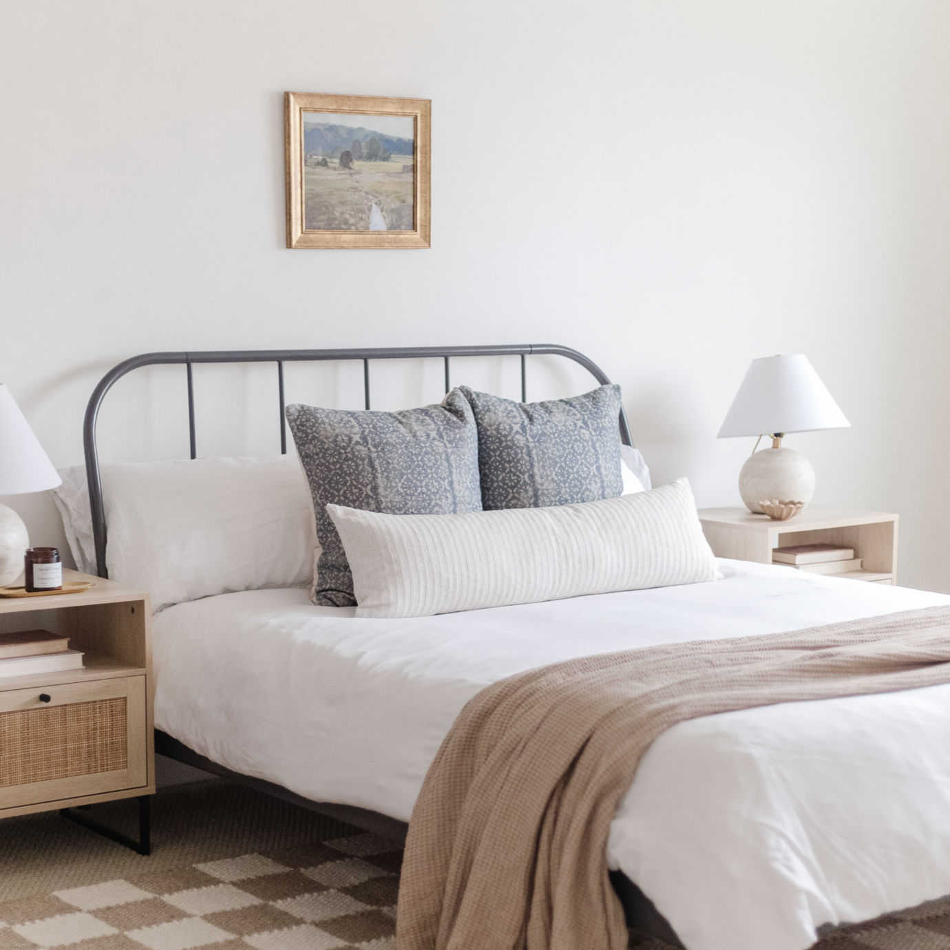 Wooden framed landscape print with mountain and field scene hung above metal bed frame.