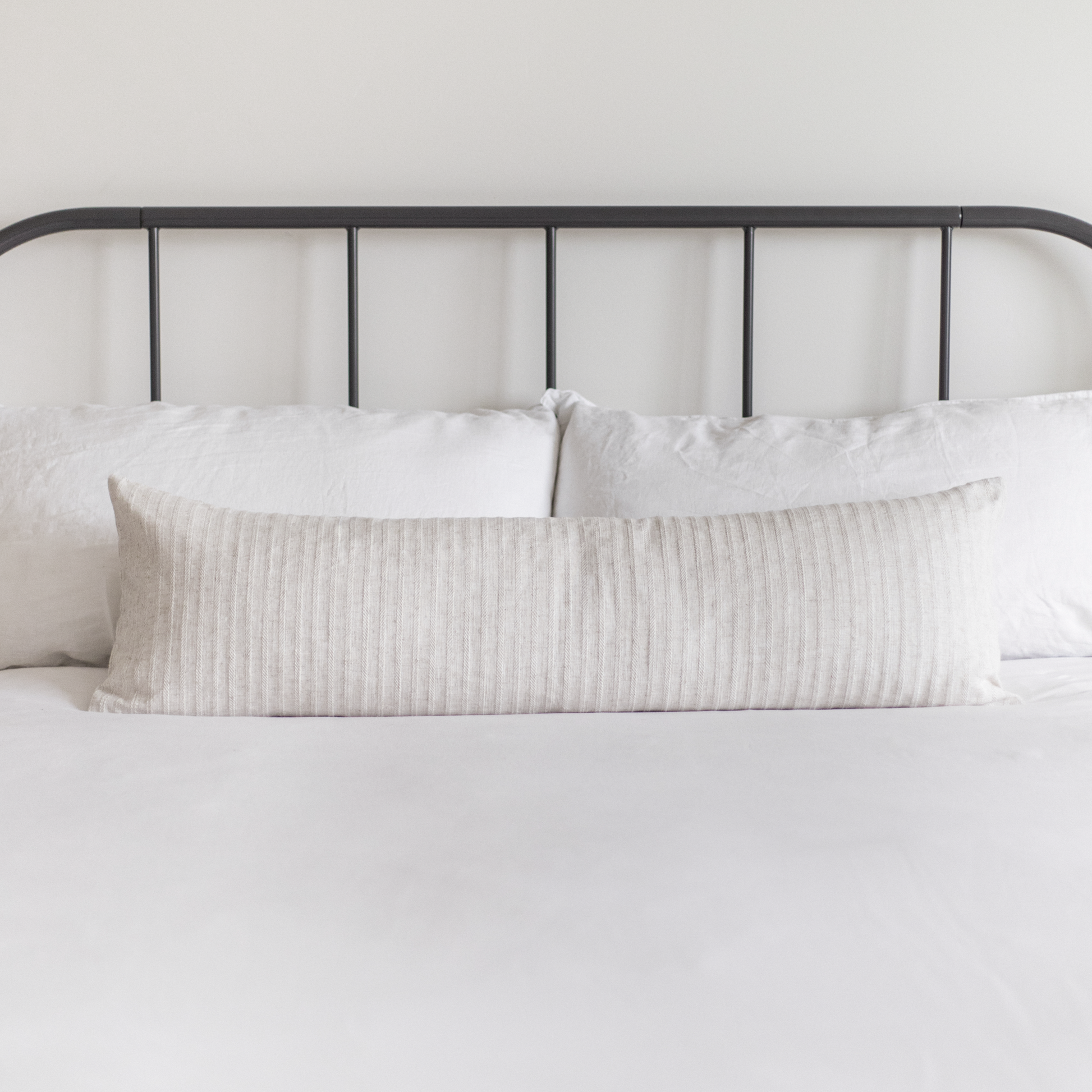 Cream ribbed lumbar pillow on bed with white bedding and black metal headboard.