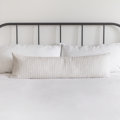 Cream ribbed lumbar pillow on bed with white bedding and black metal headboard.