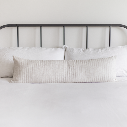 Cream ribbed lumbar pillow on bed with white bedding and black metal headboard.