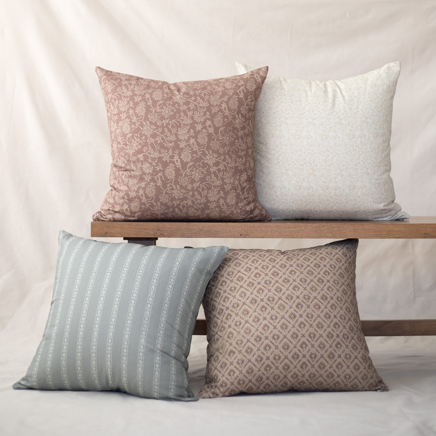 Four decorative pillows in varying patterns: mauve floral, cream solid, sage striped, and taupe geometric designs.