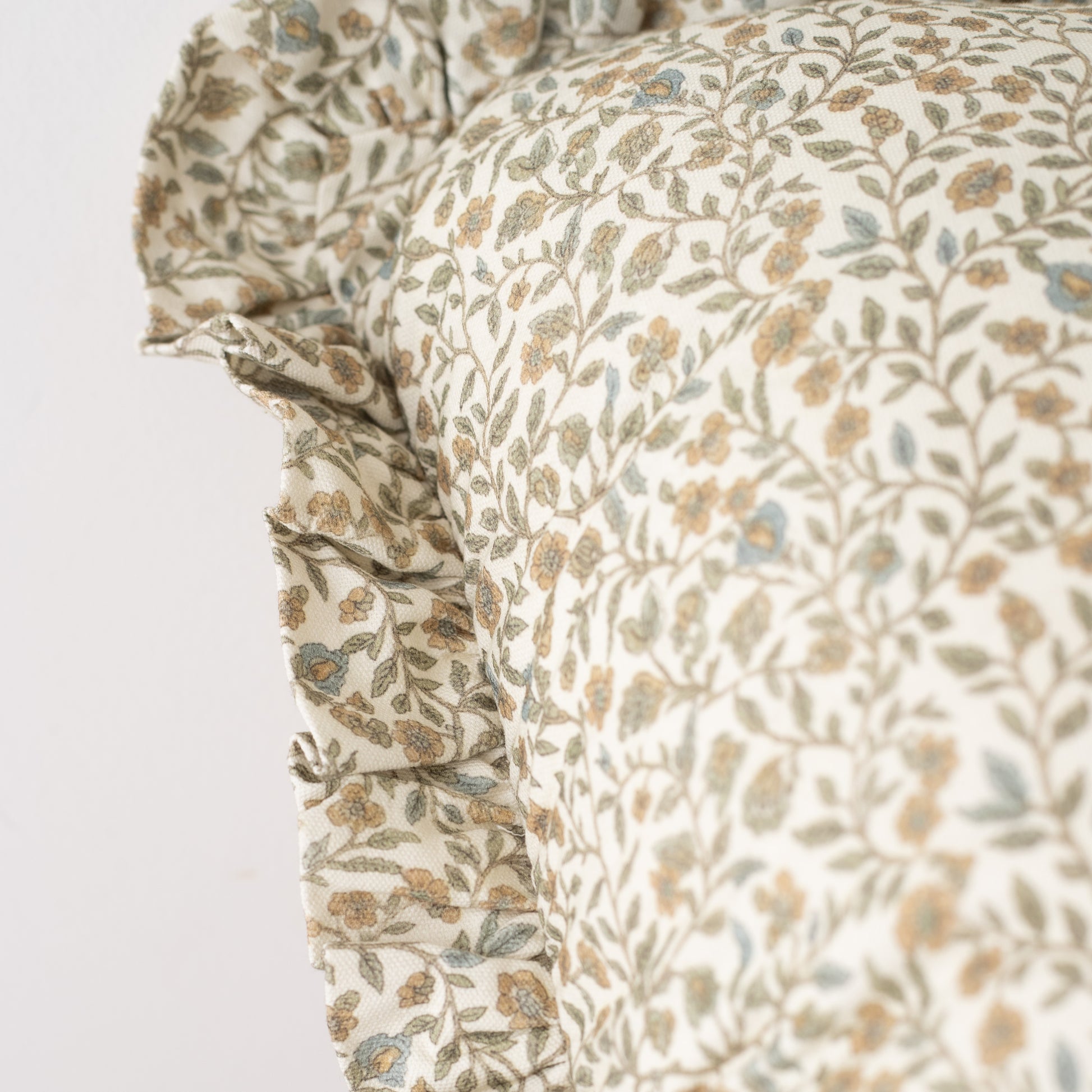 Cream pillow with tan and blue floral leaf pattern and ruffled edge detail.