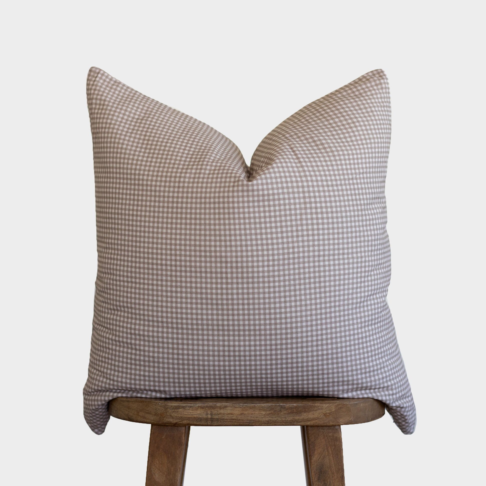 Tan and white gingham check pillow cover displayed on wooden stool against neutral background.