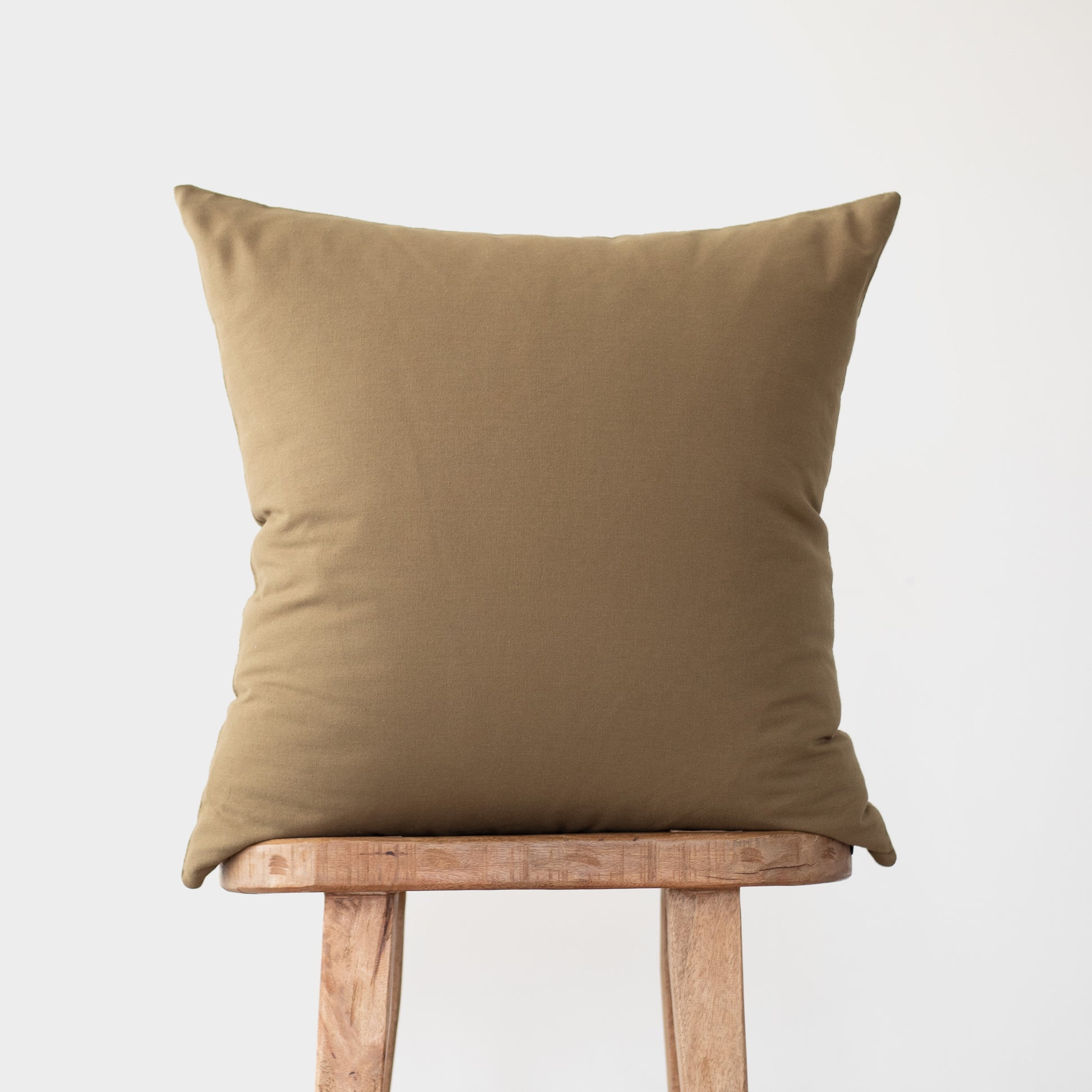 Tan linen square pillow displayed on a wooden stool against a gray background.
