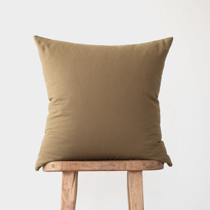 Tan linen square pillow displayed on a wooden stool against a gray background.