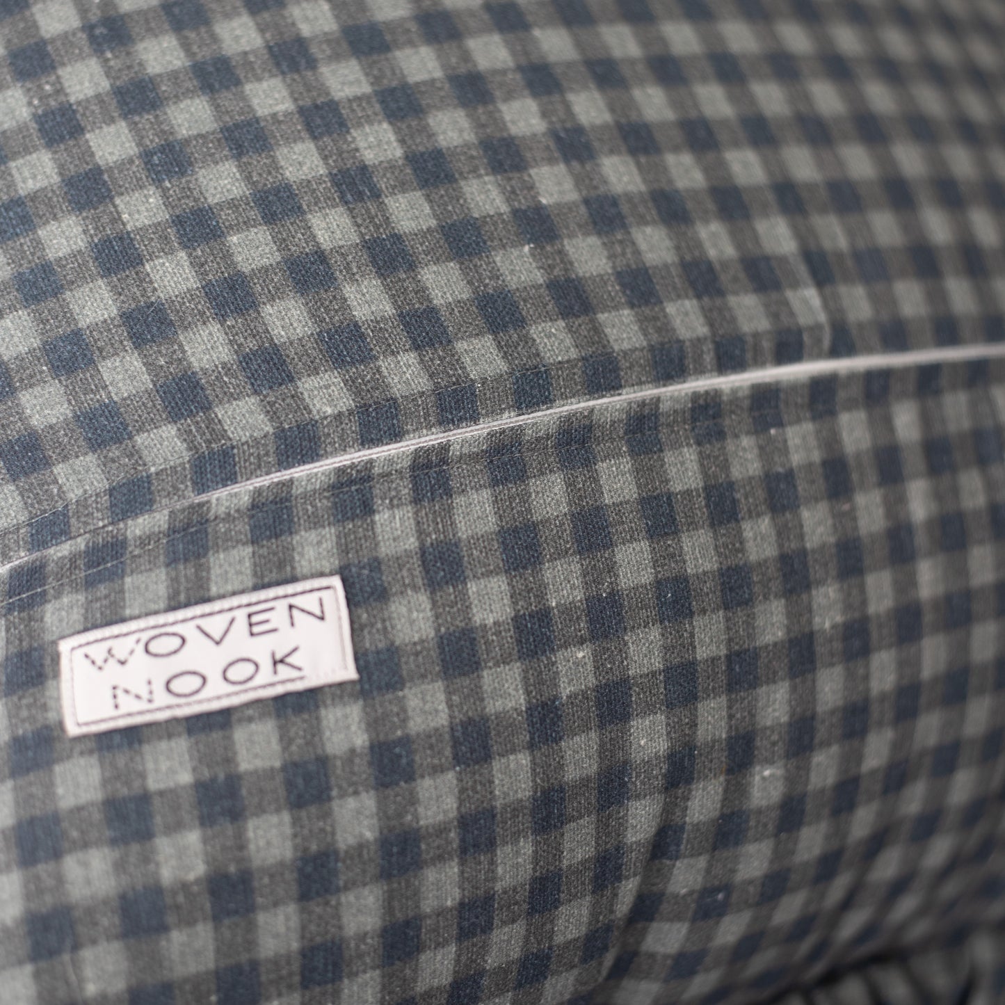 Navy and white gingham pillow with ruffle edge and brand label visible.