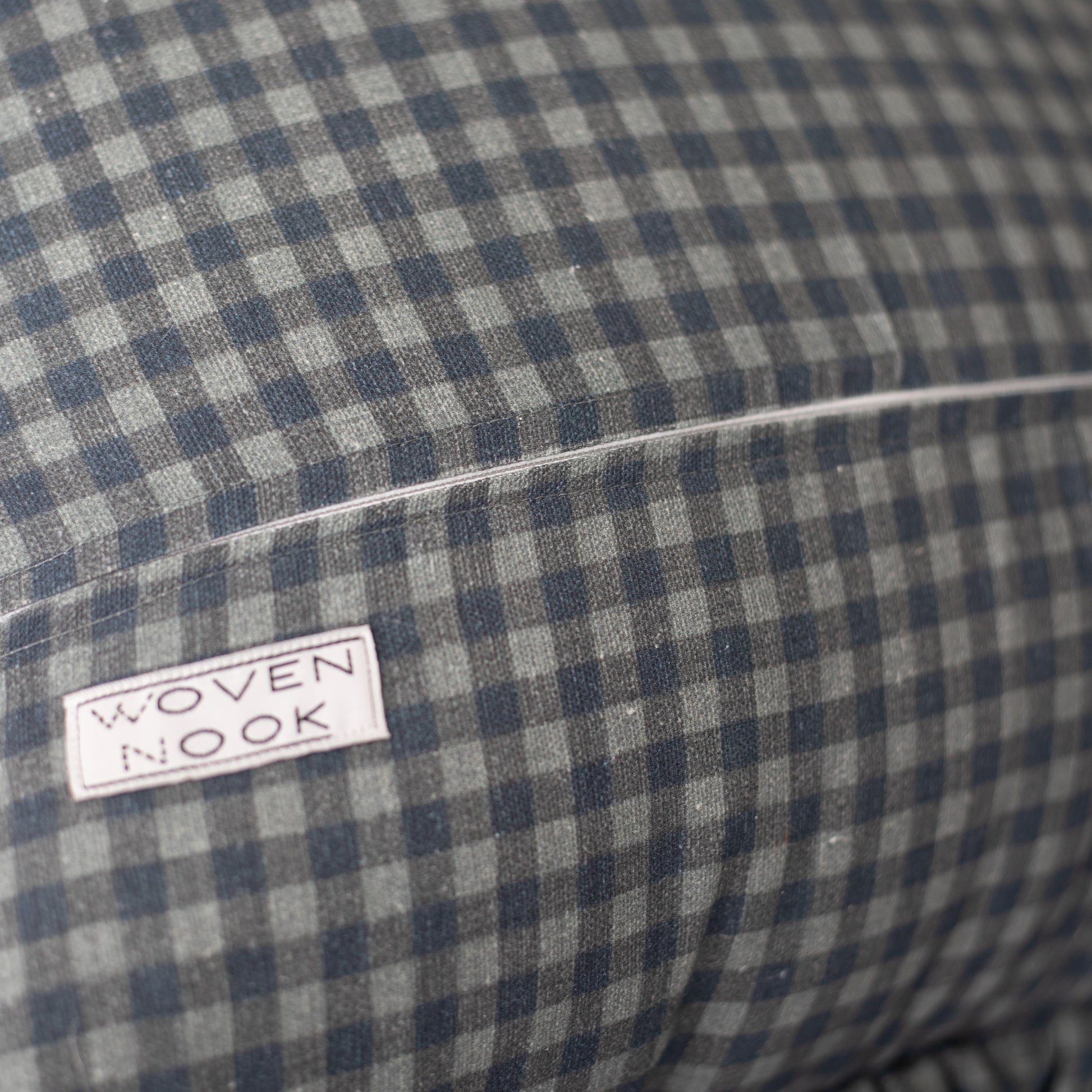Navy and white gingham pillow with ruffle edge and brand label visible.