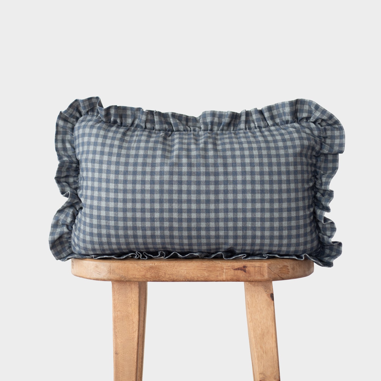 Navy gingham pillow with ruffled edges on all sides, displayed on wooden stool.