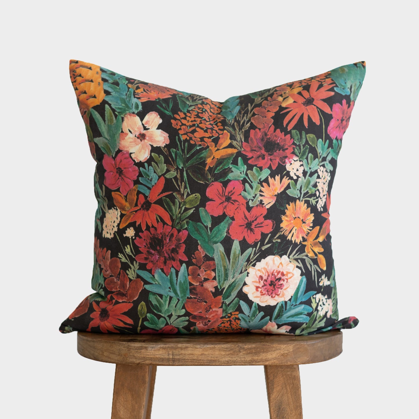Dark floral throw pillow with red, orange, pink, and cream flowers on black background with teal foliage.