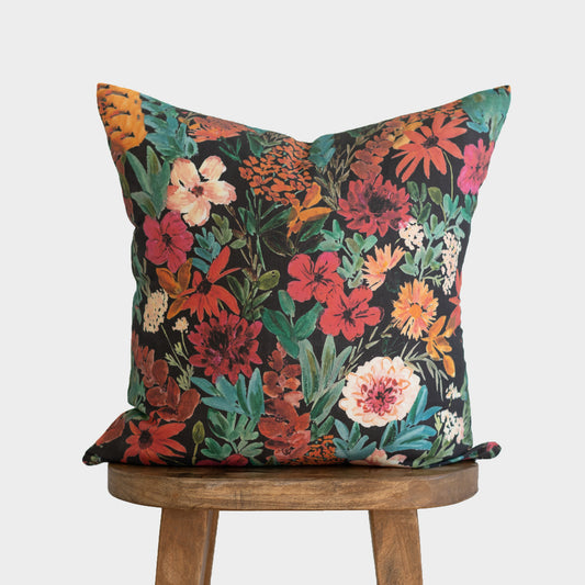 Dark floral throw pillow with red, orange, pink, and cream flowers on black background with teal foliage.