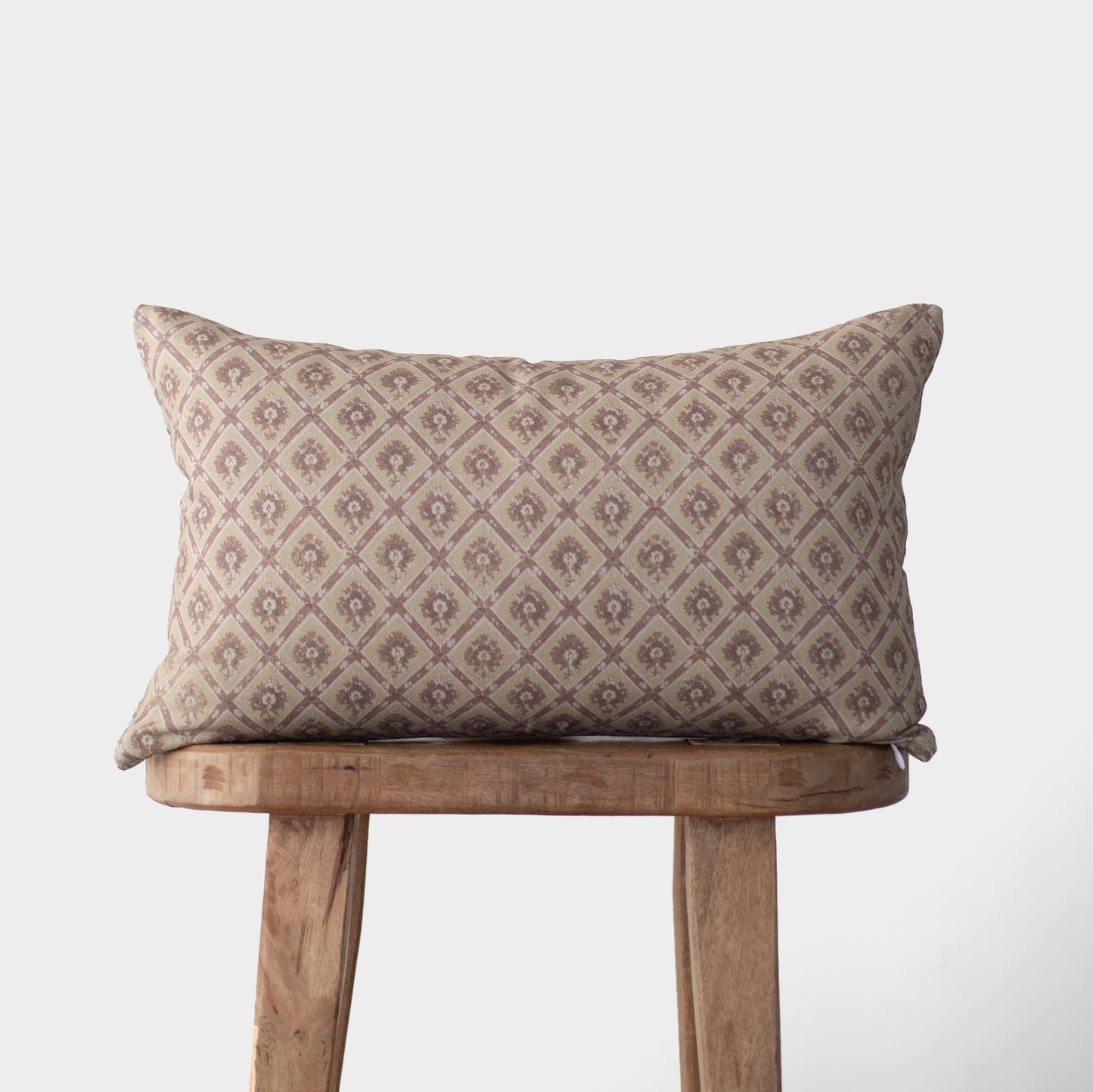 Noa pillow with geometric diamond pattern in taupe and cream tones on wooden stool.