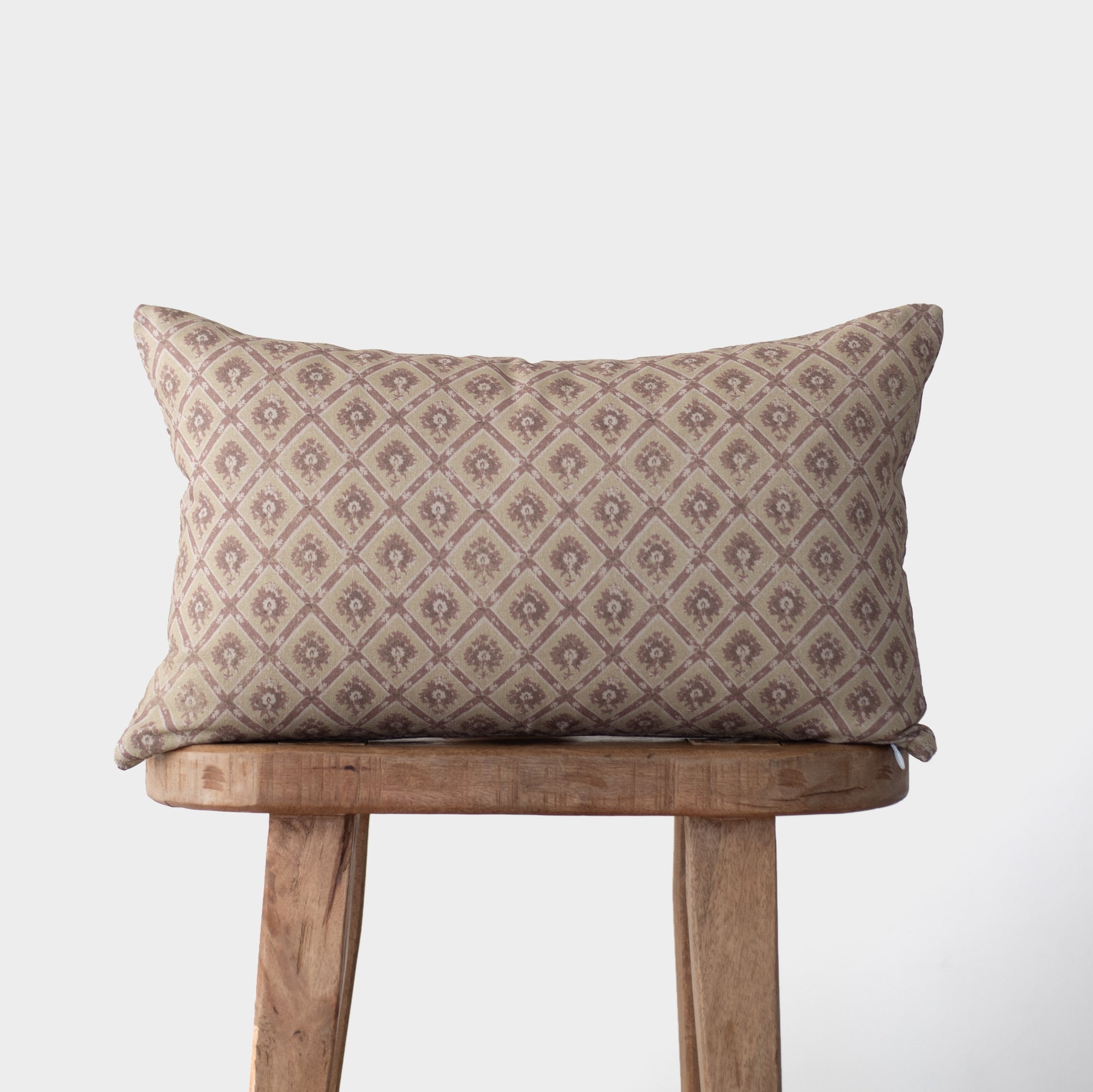 Noa pillow with geometric diamond pattern in taupe and cream tones on wooden stool.