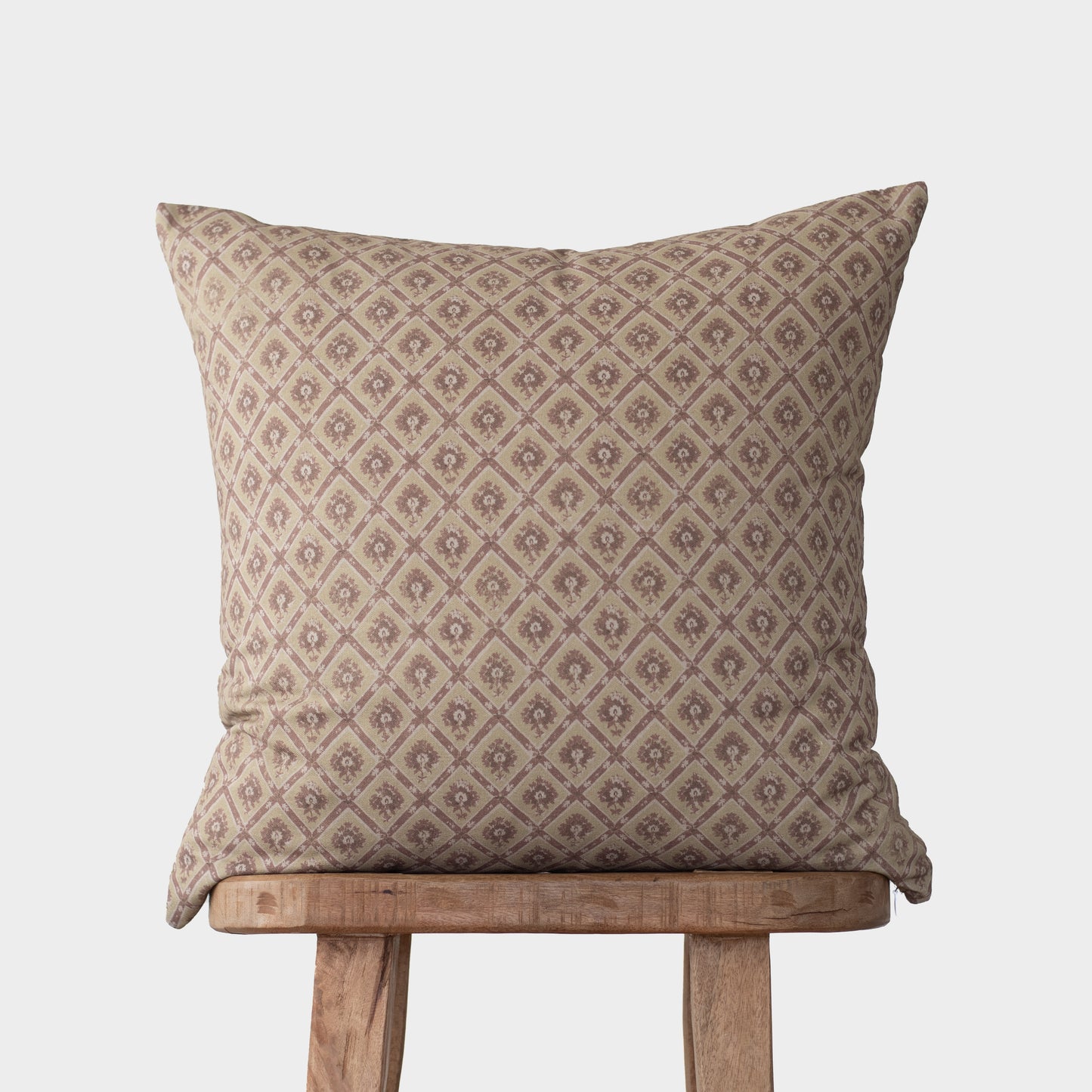 Beige pillow with diamond and floral geometric pattern, displayed on wooden stool.