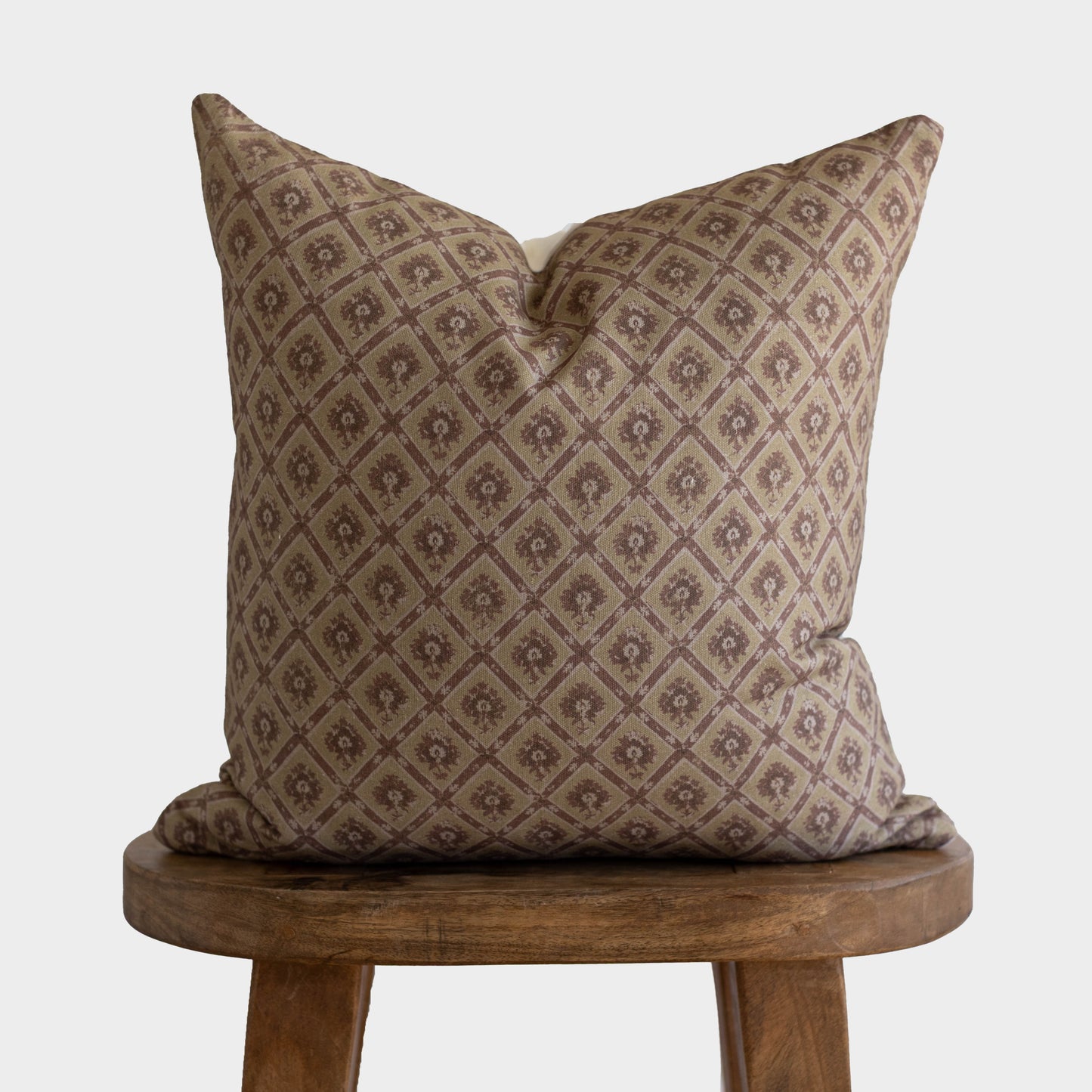 Tan and brown diamond patterned pillow with small floral motifs displayed on a wooden stool.