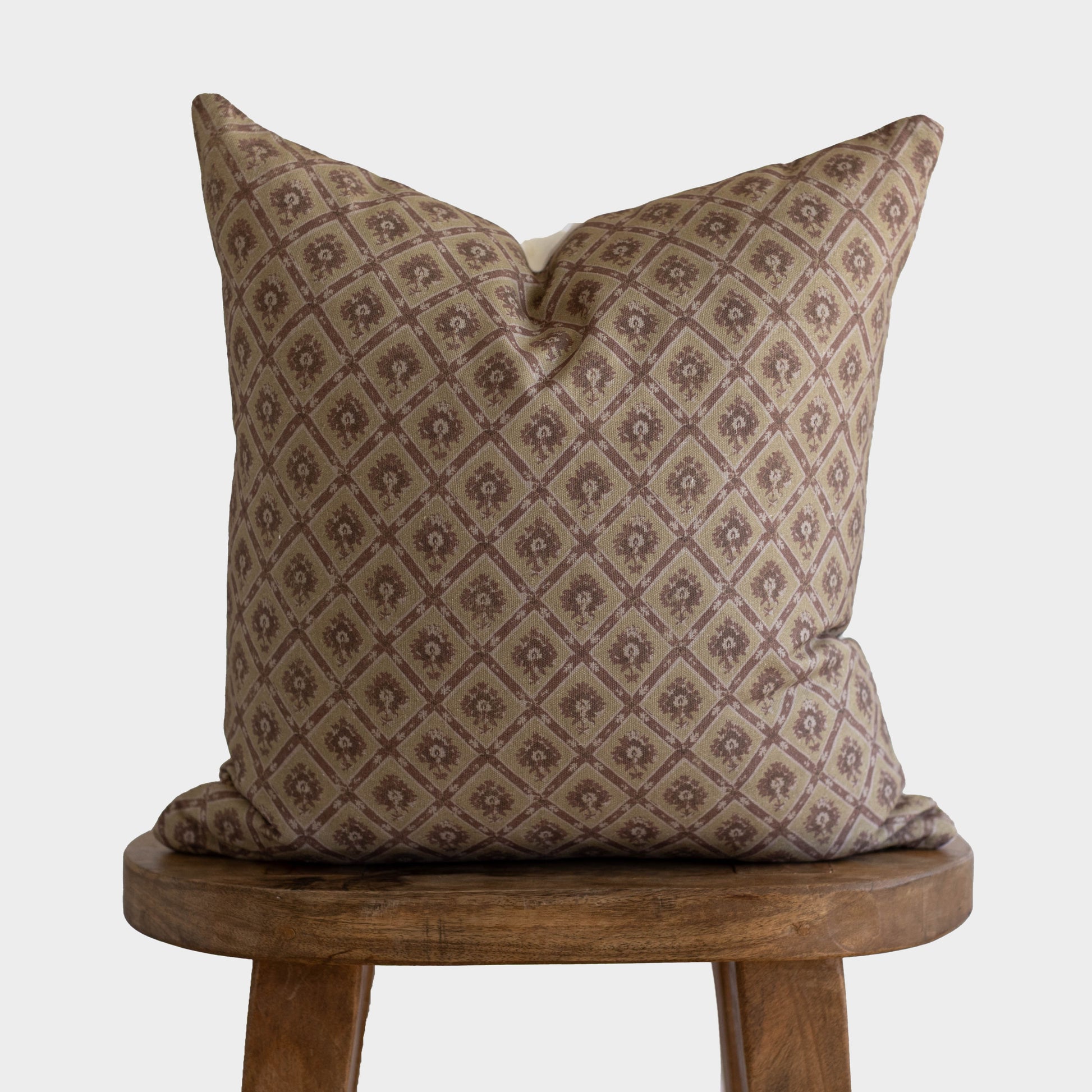 Tan and brown diamond patterned pillow with small floral motifs displayed on a wooden stool.