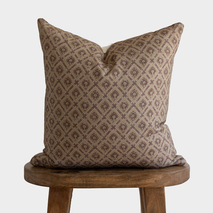 Tan and brown diamond patterned pillow with small floral motifs displayed on a wooden stool.
