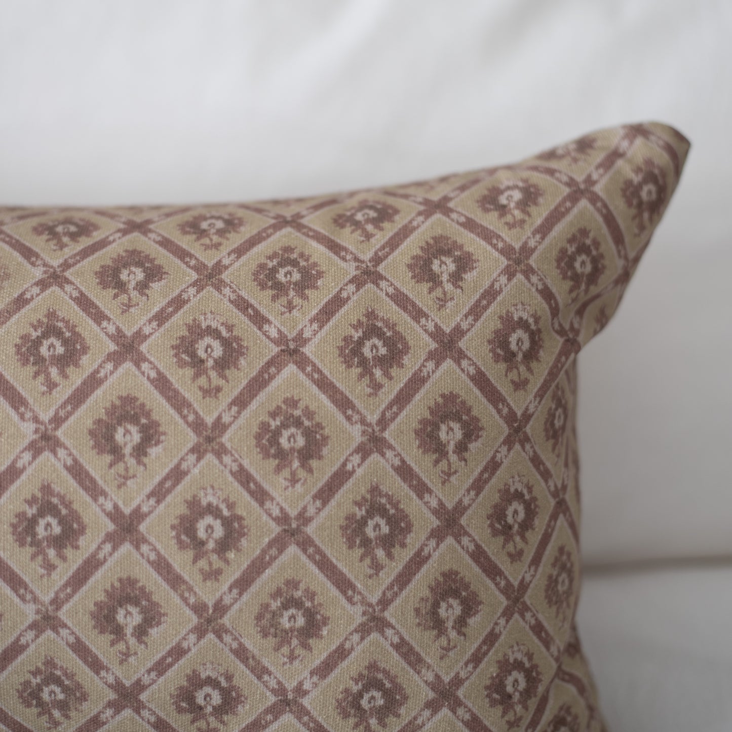 Rectangular pillow with mauve and cream diamond grid pattern containing small floral motifs.