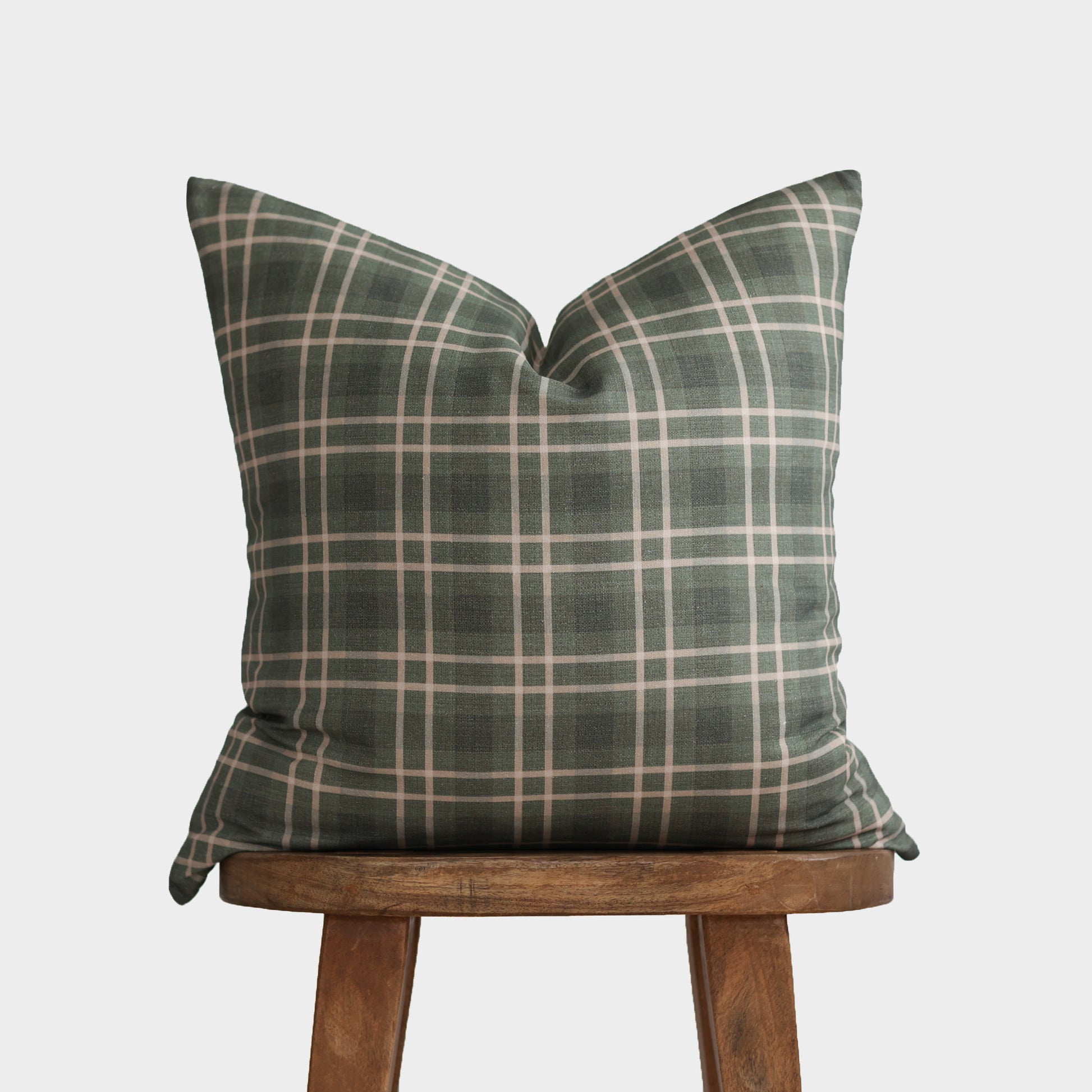 Green and cream plaid pillow with envelope closure displayed on wooden stool.