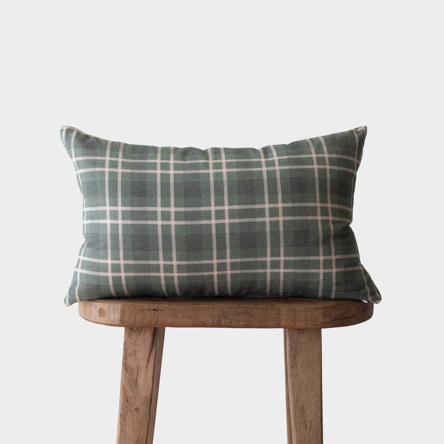 Gray and white plaid lumbar pillow on wooden stool against neutral background.
