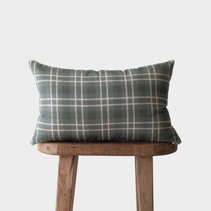 Gray and white plaid lumbar pillow on wooden stool against neutral background.