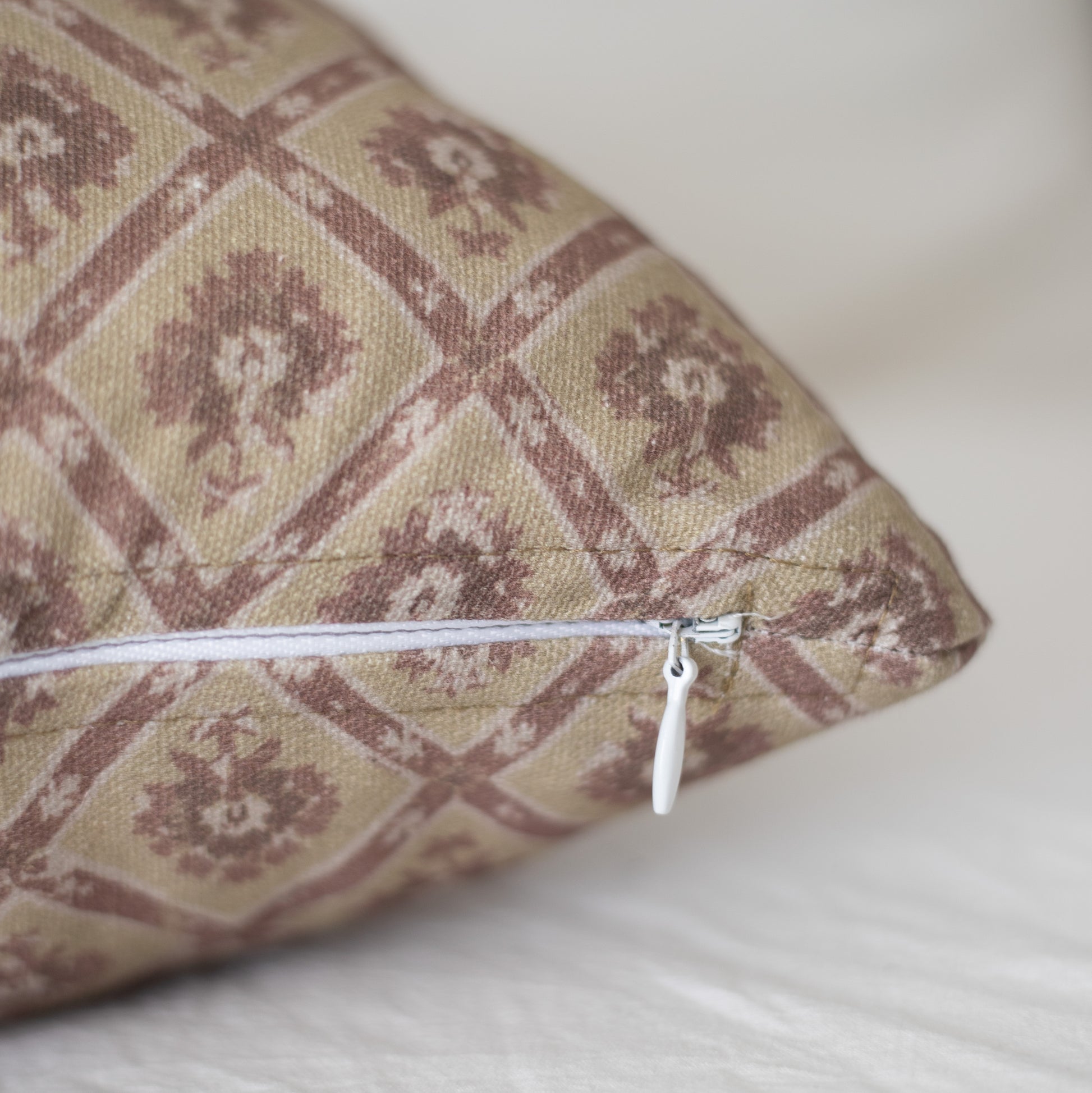 Beige and burgundy patterned throw pillow with geometric design and white zipper closure.