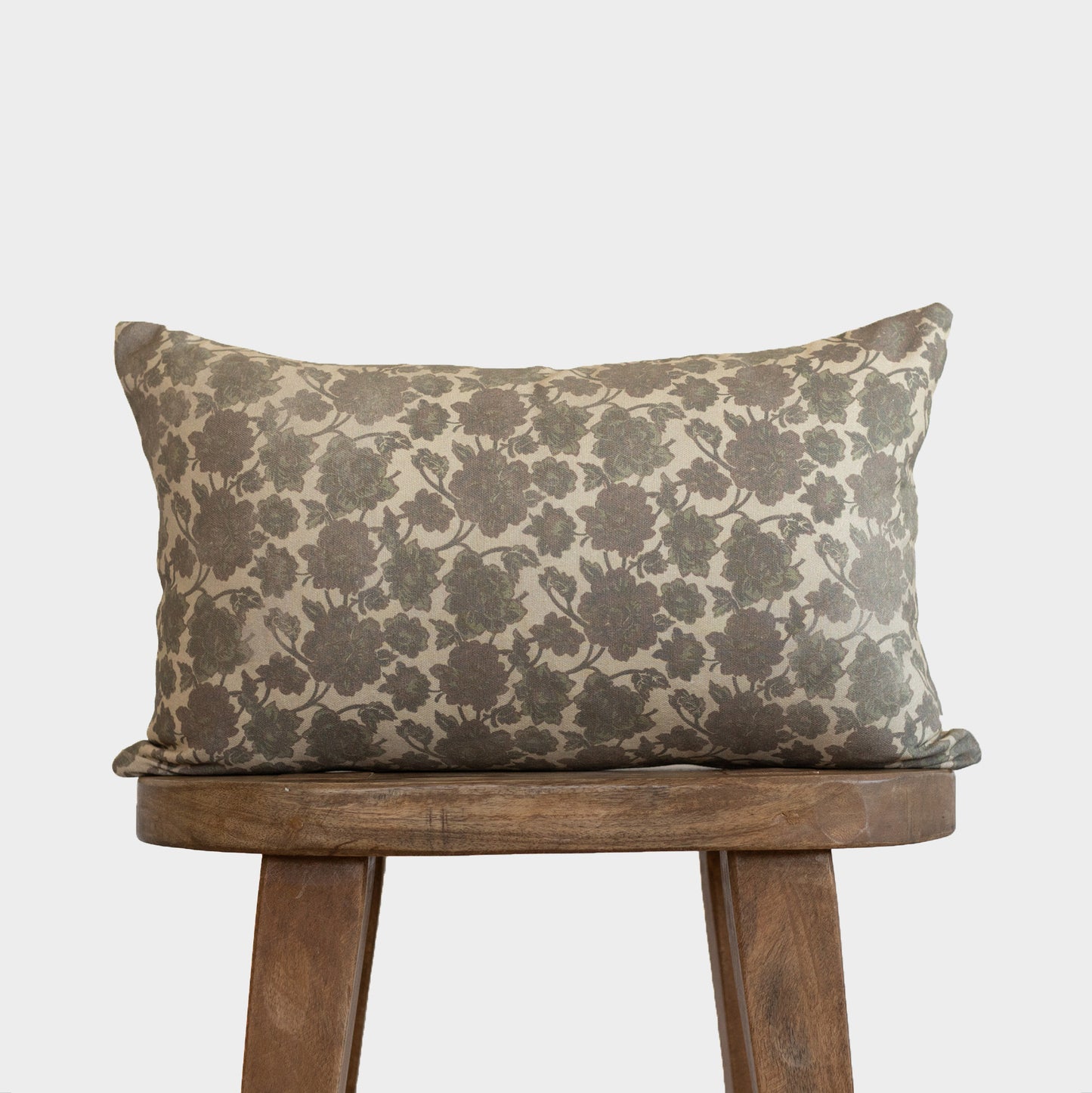 Rectangular lumbar pillow with gray floral damask pattern on cream background, displayed on wooden stool.
