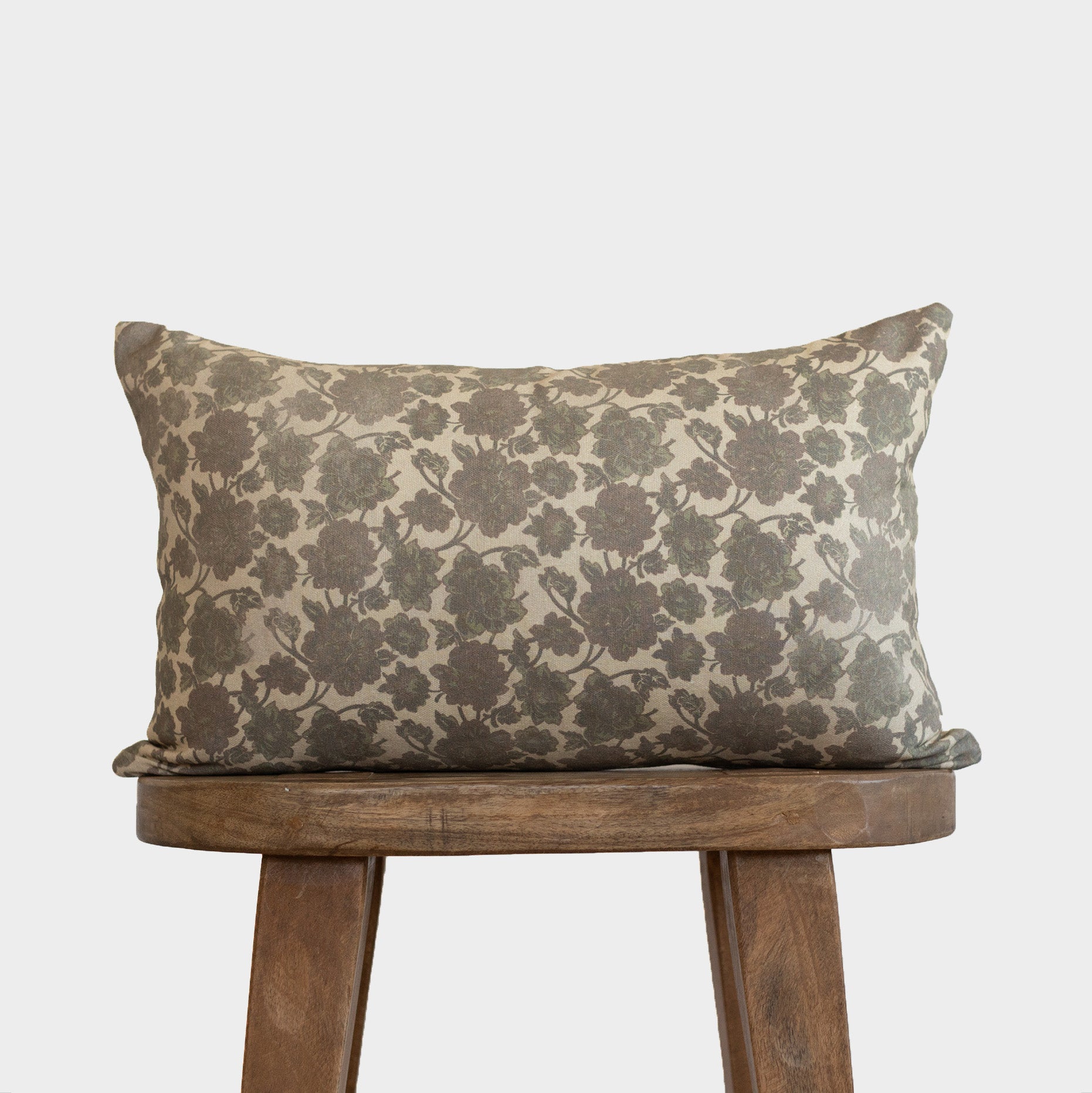 Rectangular lumbar pillow with gray floral damask pattern on cream background, displayed on wooden stool.