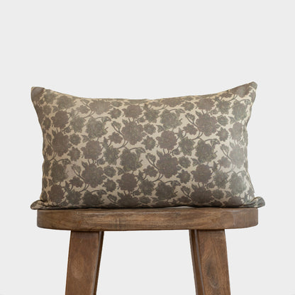 Rectangular lumbar pillow with gray floral damask pattern on cream background, displayed on wooden stool.