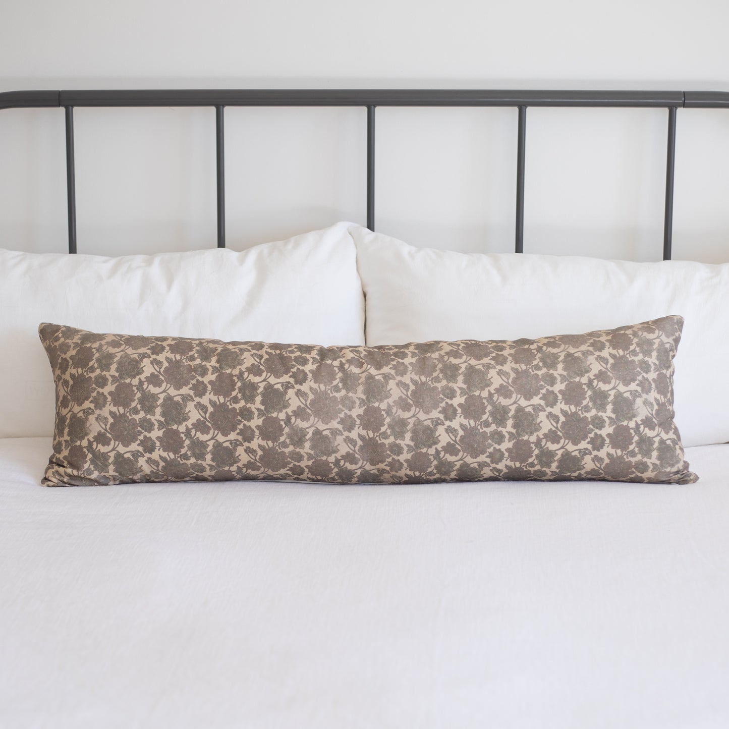 Nora lumbar pillow with tan damask pattern on white bedding against metal headboard.