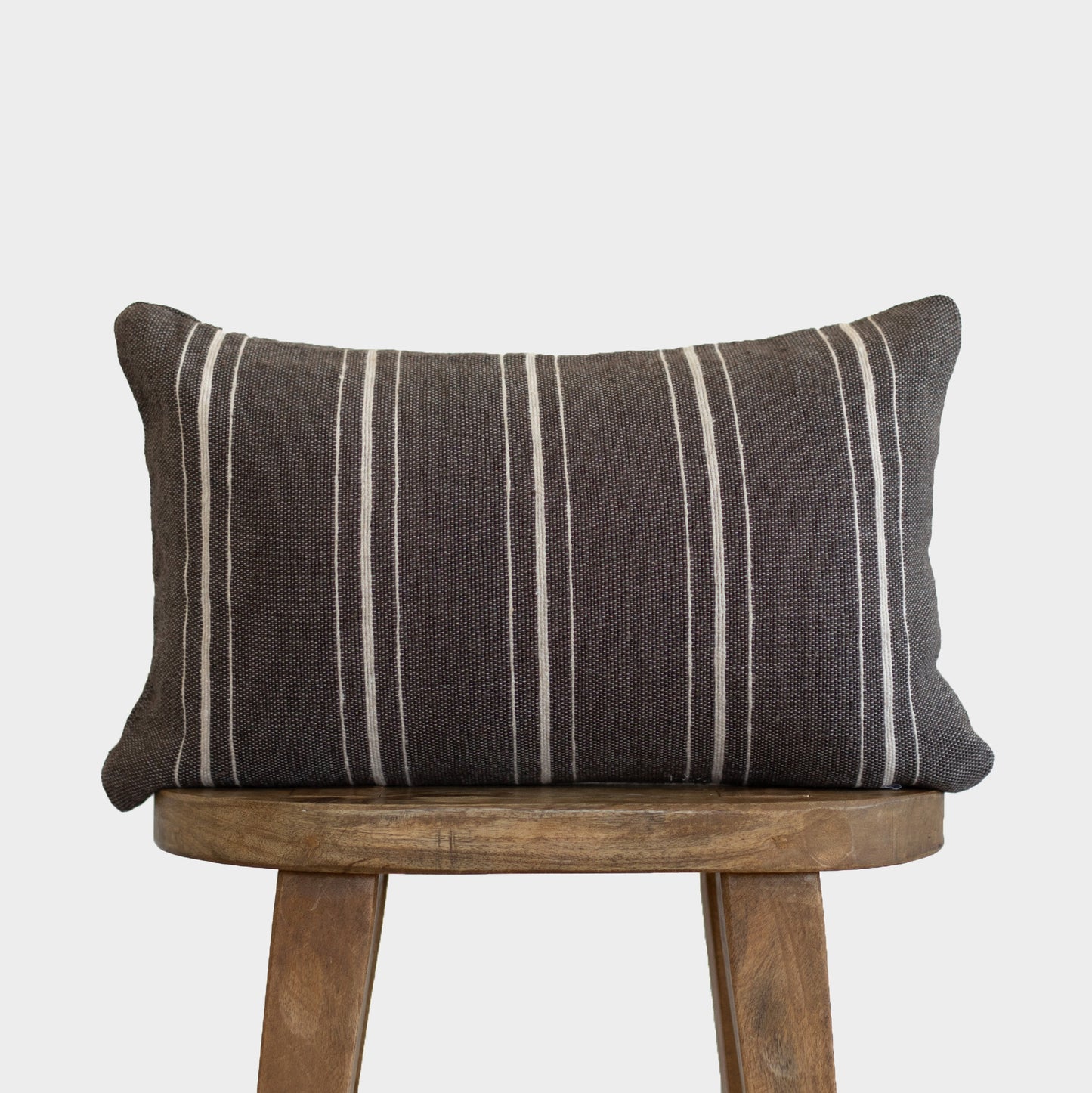 Charcoal lumbar pillow with white vertical stripes on wooden stool.