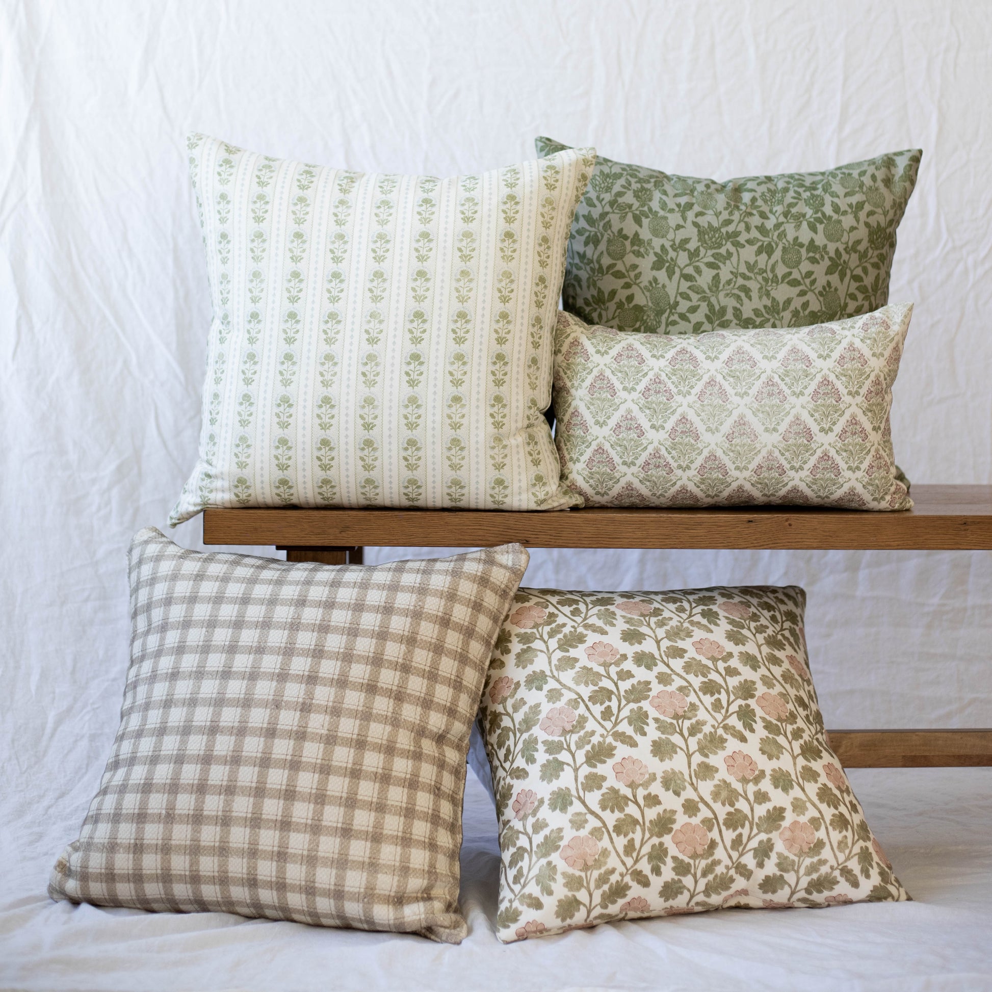 Five decorative pillows in various patterns including stripes, florals, and geometric designs in green, cream, and tan tones.
