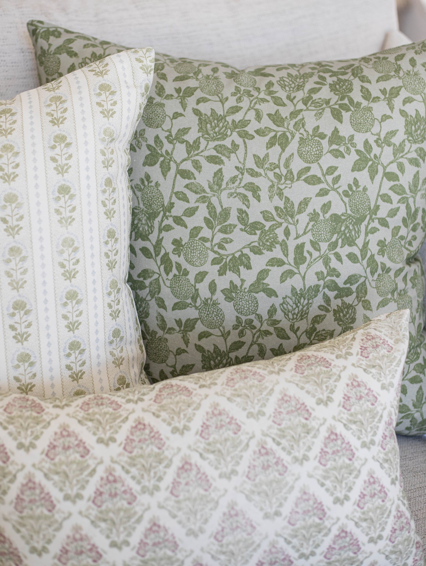 Five decorative pillows with green botanical and pink floral patterns in varying sizes.